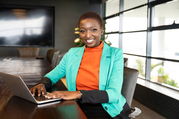 front view of corporate professional in vibrant attire sitting at conference table and pausing from typing to smile at camera. (2)